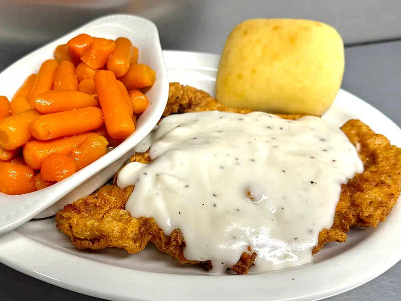 Country fried steak smothered in white pepper gravy with a dinner roll