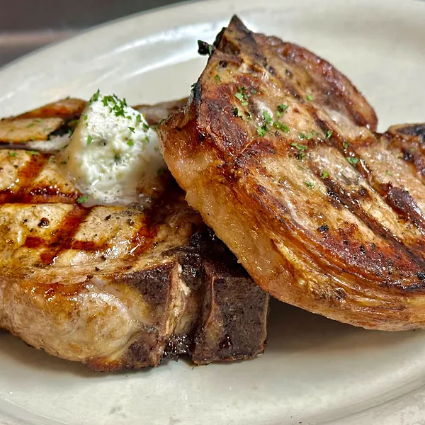 Two thick char-grilled pork chops topped with garlic butter