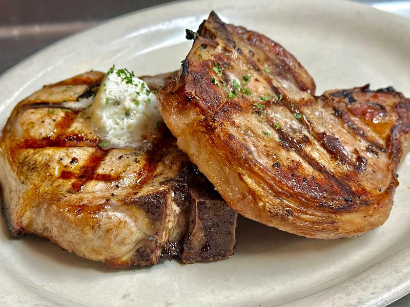 Two thick char-grilled pork chops topped with garlic butter