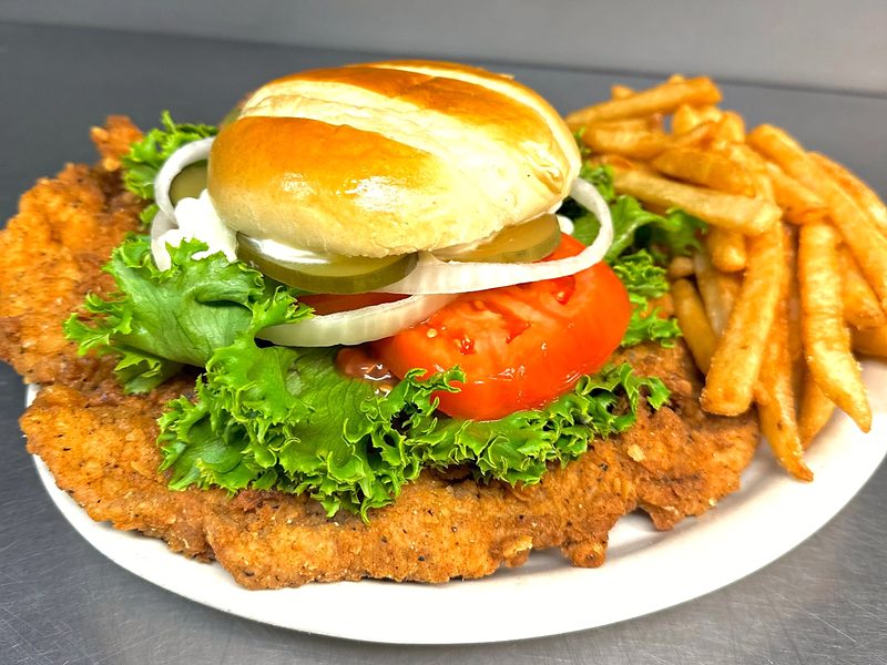 A Hoosier-style breaded pork tenderloin sandwich, bigger than its bun, with steak fries